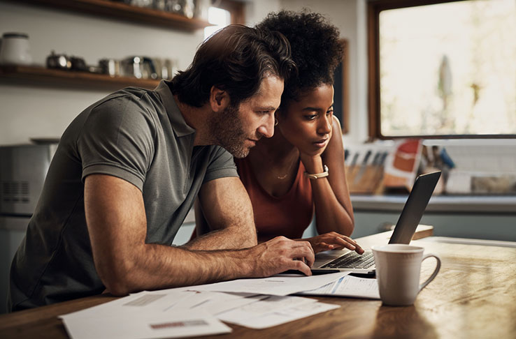 a couple reviewing their finances in a kitchen using a laptop, with paperwork on a table