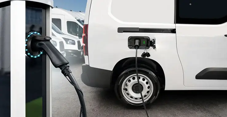 A white electric van connected to a public charging station.