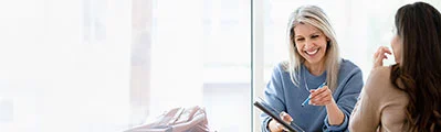 smiling female consultant reviewing documents at her desk on a digital tablet sitting opposite her client.