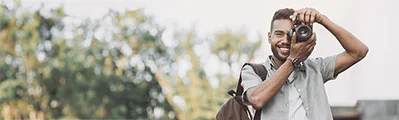 A smiling photographer is outdoors taking a photo with his camera.