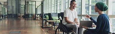 A teacher is talking and sharing her laptop screen with a disabled student in a college.