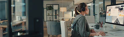 side view of a designer wearing headphones while working on a computer in an office.