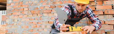 bricklayer wearing a safety helmet laying red bricks on a construction site.